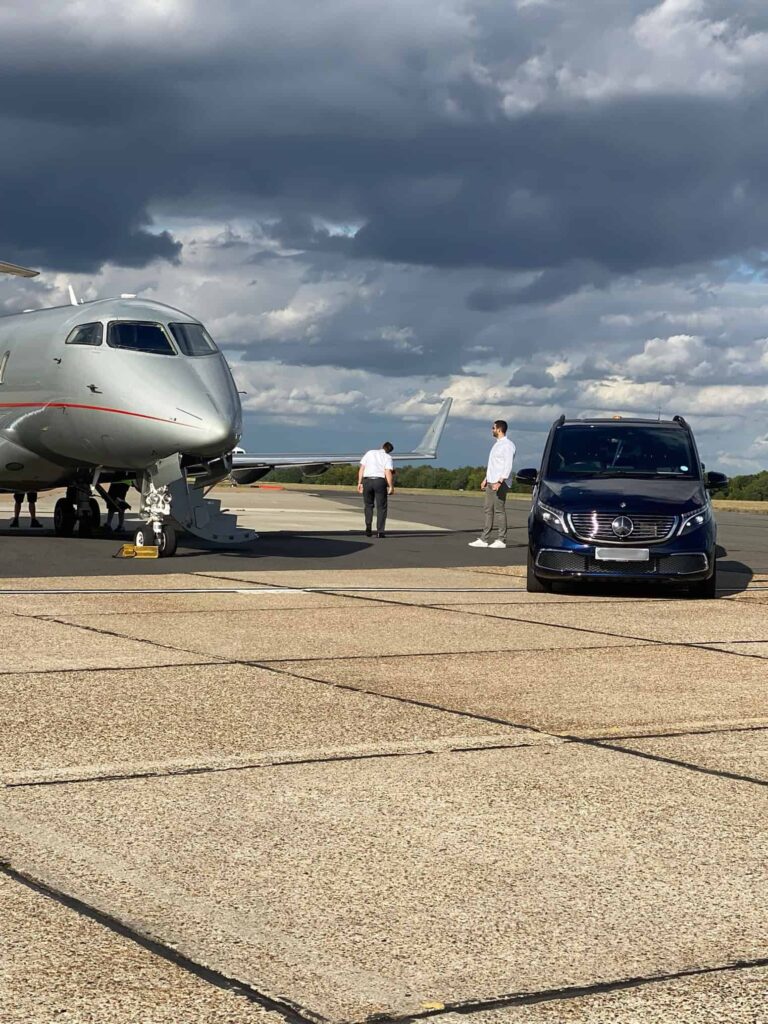 A private jet on the tarmac next to a black van with people walking between them.