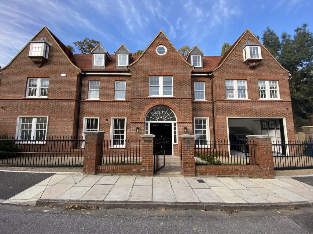 A large red-brick mansion with symmetrical architecture and a gated front entrance.